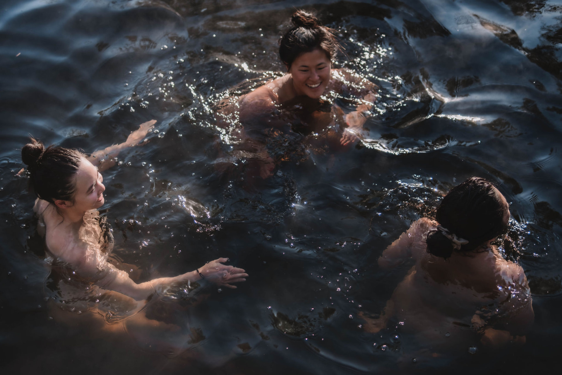Women swimming together in dark sunlit water
